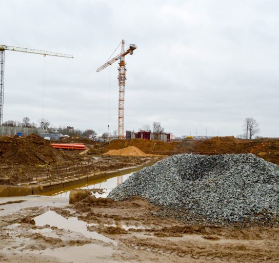 A large modern construction site in the construction of buildings and houses with appliances and many large high tower and stationary industrial powerful cranes and building materials.