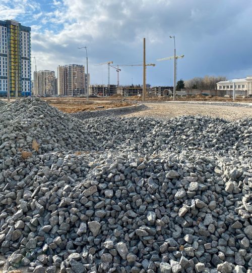 Large gray stones, rubble from industrial road construction and a view of new buildings with cranes at the construction site.