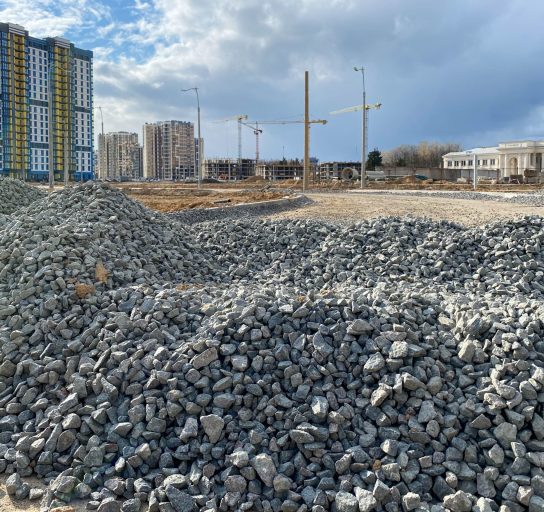 Large gray stones, rubble from industrial road construction and a view of new buildings with cranes at the construction site.